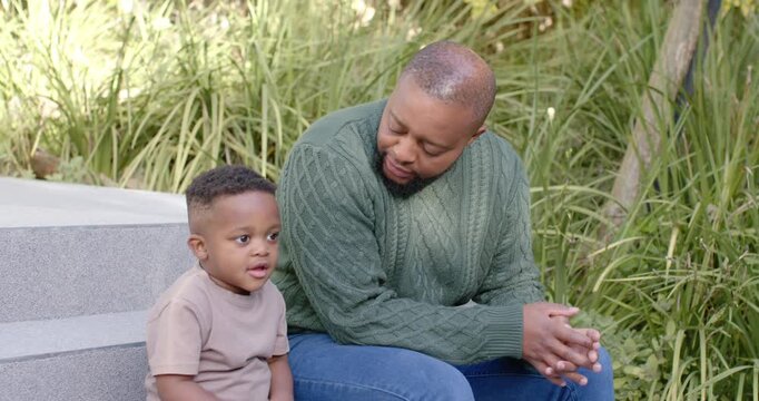African American father and son sitting on steps, child talking, fiddling, father leaning to soothe