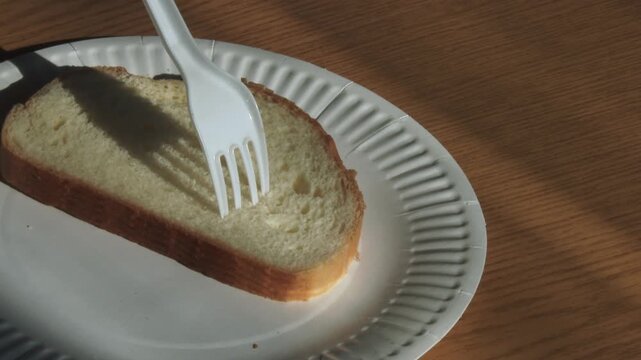 Zoom on a plastic fork stuck into bread on a paper plate in warm light.