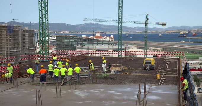 Timelapse of construction workers pouring concrete from a hose, then spreading, vibrating and smoothing it over steel rebar on a building floor