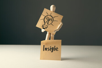 A wooden mannequin holding a light bulb on a note with the word insight © Artvibe