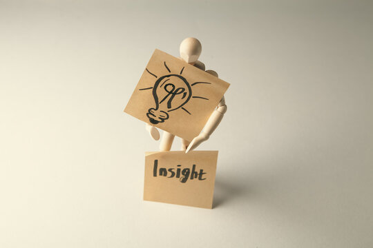 A wooden mannequin holding a light bulb on a note with the word insight