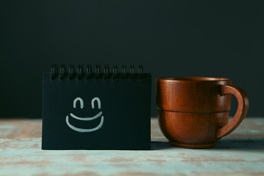 Cup of coffee and blackboard with smiley face on wooden background