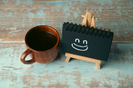 Cup of coffee and blackboard with smiley face on wooden background