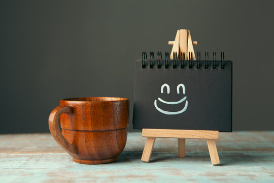 Cup of coffee and blackboard with smiley face on wooden background