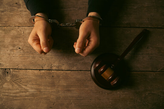 Handcuffs and judge gavel on wooden table, top view