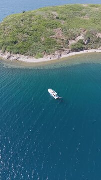 Aerial view of motorboat anchored near green coast of Cunda Island, Ayvalik. Vertical drone footage for summer travel and vacation. High quality 4k footage