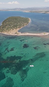 Aerial view of motorboat anchored near green coast of Cunda Island, Ayvalik. Vertical drone footage for summer travel and vacation. High quality 4k footage