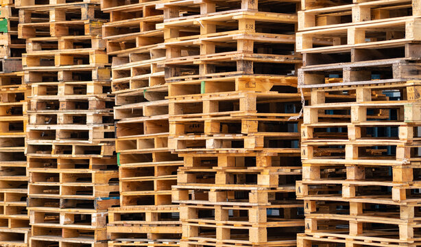 Large stacks of used wooden pallets stored at an industrial warehouse, ready for cargo shipping, freight handling and reuse within sustainable logistics and supply chain operations. Reusable packaging