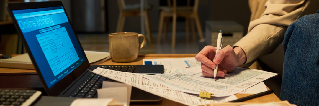 Header of Caucasian young adult filling out financial tax documents near laptop showing online banking interface. Concept depicts home accounting, commercial budgeting and fintech service banner