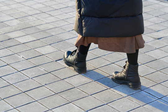Woman in black leather boots taking steps on dry city sidewalk treated with white rock salt for anti slip winter traction