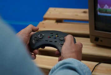 Hands holding a retro game controller while playing a video game on a classic monitor. Nostalgic gaming scene with selective focus, vintage technology and a softly blurred background. © Dr. CraftLab