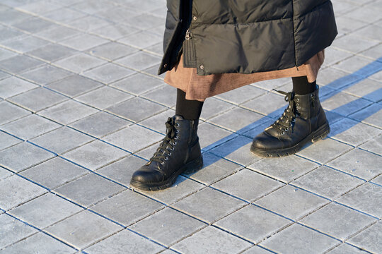 Female legs in black leather boots stepping on dry paving tiles covered with white rock salt residue and grit for winter traction. Person in black leather boots walking on salted sidewalk