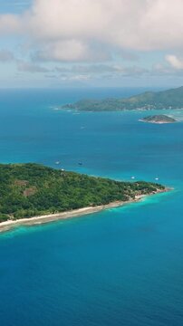 Island coastline with blue ocean waters, bordered by green hills under a clear sky. La Digue, Seychelles.