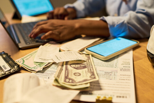 African American adult calculating personal budget, using laptop near paper bills and money. Scene representing personal finance management for banking and tax service marketing