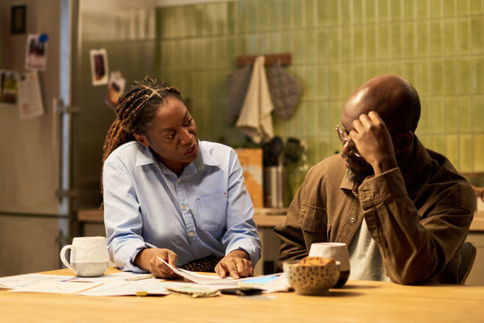 African American couple discussing financial documents and bills at home, managing debt and household budget. Image suitable for banking, debt relief, loans marketing