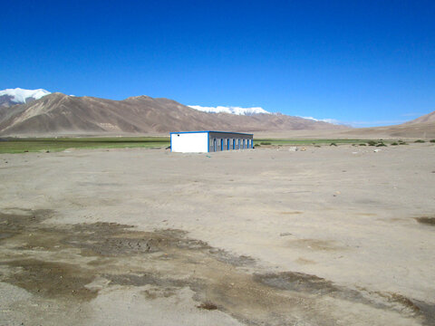 A solitary building in a vast open desert landscape with mountains in the background