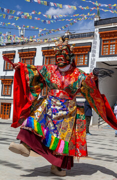 Cham dance with masked lamas as a dancer in red mask and brocade robe spins in a monastery courtyard, Ladakh, Leh, India