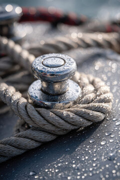 Water covered metal mooring bollard with thick braided rope on a wet boat deck in soft focus maritime harbor setting