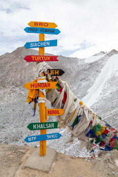 Colorful wooden signpost with direction arrows and prayer flags on a snowy mountain pass, Ladakh, Turtuk, India
