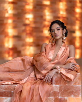 Woman in coral kimono lying on blocks of Himalayan pink salt in salt cave sanctuary. Halotherapy, speleotherapy and respiratory wellness concept. Fashion portrait for alternative medicine poster