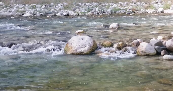 Clear mountain river flowing around boulders with white foam