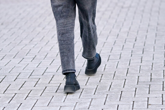 Female legs in black leather boots and grey jeans walking on dry paving tiles covered with white rock salt residue for winter traction. Woman in boots walking on paved tiles dusted with deicing salt
