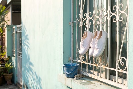 Freshly whitened canvas school shoes drying on a window grille