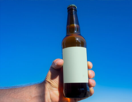 Amber beer bottle mockup with a blank pale green label held against blue sky