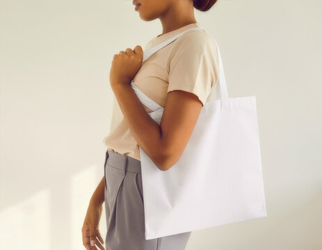 Blank white tote bag mockup carried by a person in a beige t shirt