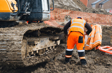 Construction worker inspects excavator tracks at a muddy work site © Iryna