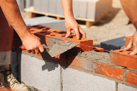 Worker lays red bricks on a concrete block wall at a construction site