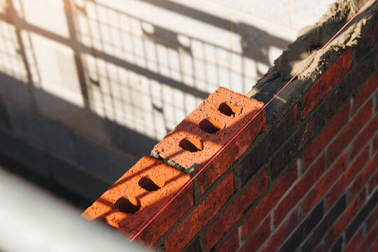 Bricklayer aligns a red brick course on a wall at a construction site