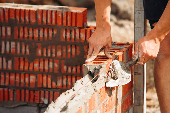 Mason lays red bricks with mortar at a building site
