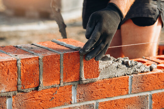 Mason places a brick along a guide line while building a wall
