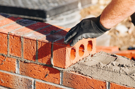 Bricklayer aligns a perforated brick on a mortar bed at a building site