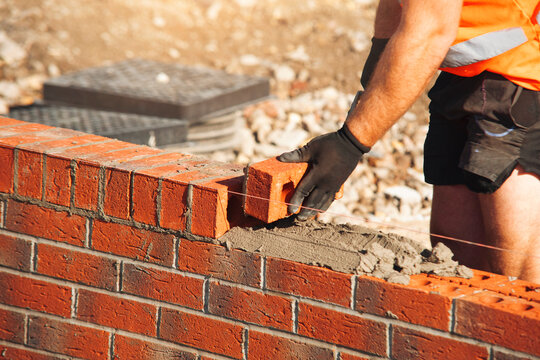 Construction worker placing a brick along a guide line at a building site