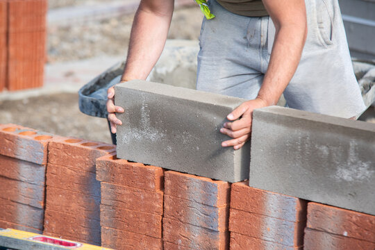 Worker places concrete blocks on a brick wall during construction