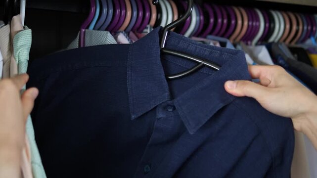 Close up of hands browsing and selecting shirts in a wardrobe closet