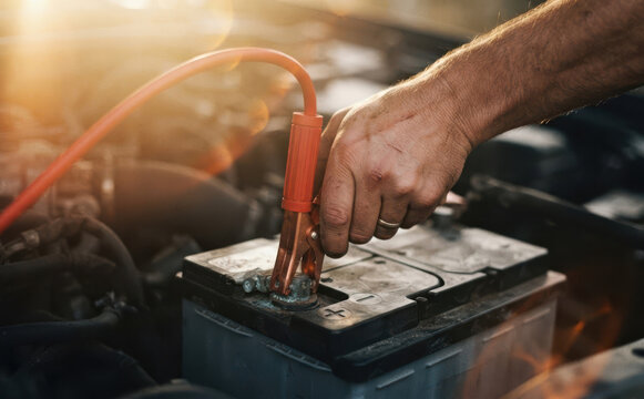 Mechanic man using jumper cables to jump start a car battery in engine compartment