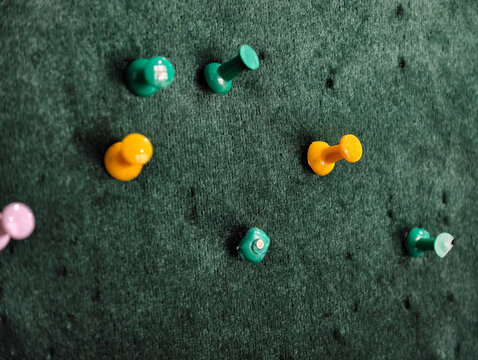 Close-up of colorful push pins thumbtacks pinned on a green felt notice board. Ideal for office supplies, education, school, reminder, planning, and business organization concepts.