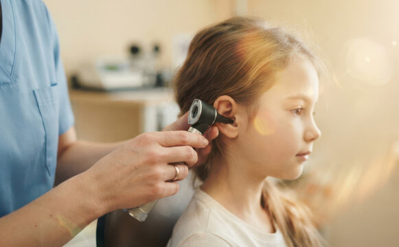 Pediatrician examining young Caucasian girl ear with otoscope in medical clinic for health checkup