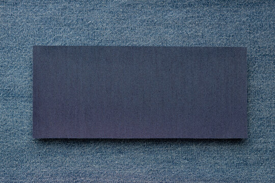 Blank dark denim fabric rectangle on blue jeans textile background. Clothing and apparel material sample for clothing and fashion design with copy space for branding, text