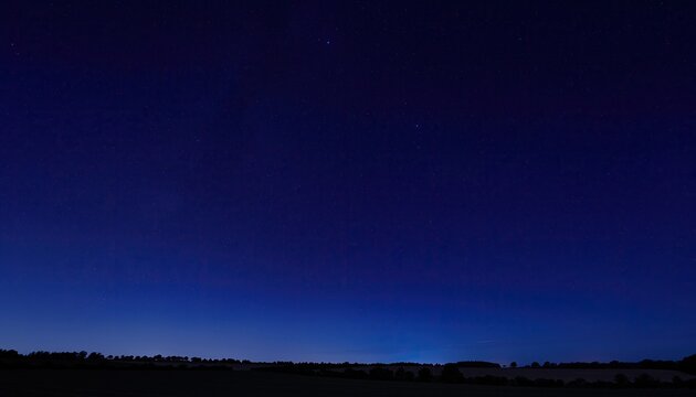 Deep blue twilight sky above silhouetted landscape, dotted with distant, faint stars