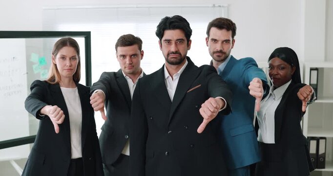 Portrait of displeased office employees group gives dislikes in corporate workplace. Multiracial team expresses negative attitude with gestures in coworking