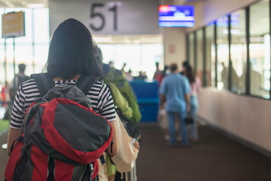 Back view of young woman tourist carrying backpack waiting in line at departure gate 51 in international airport terminal. Travel, vacation, and tourism concept. Human-created, not AI.