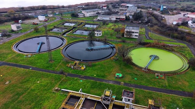 Overhead perspective of circular primary clarifiers. Large round sedimentation pools filled with treated water are surrounded by green lawns and metal walkways.