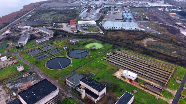 Aerial shot of rectangular aeration channels and round tanks. High angle view depicts long aeration basins circular clarifiers and industrial roofs surrounded by green grass.
