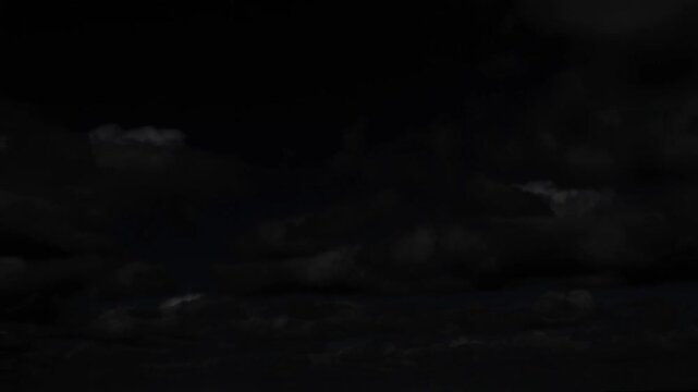 Dark clouds fill the night sky above a barely visible, dark ocean horizon