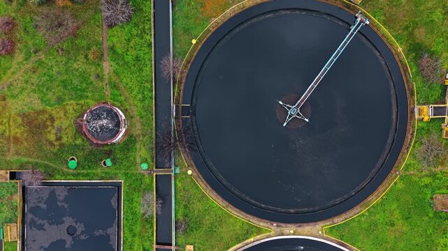 Aerial view of circular primary clarifier tank with rotating mechanism. Drone photo captures large round sedimentation pool with central metal bridge over dark liquid.