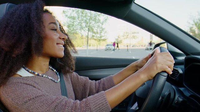 Cheerful woman moves to music while driving modern city car